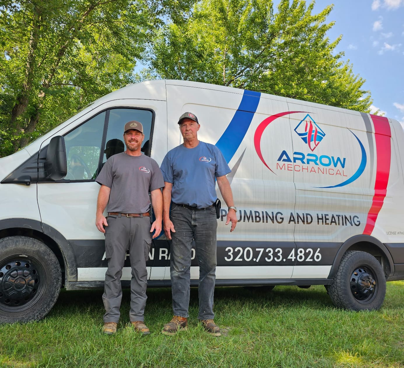 Two men stand in front of a white Arrow Mechanical van with a blue and red logo. The van advertises plumbing and heating services. Trees and a blue sky are visible in the background.